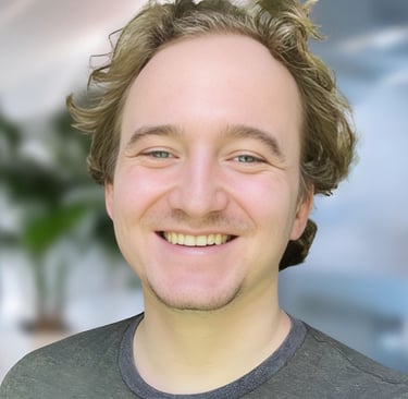 A professional headshot of a smiling man with wavy blond hair in a modern office setting.