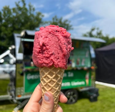 A vegan cone with one scoop of Summer Fruits sorbet ice cream. Georgio's event trailer behind