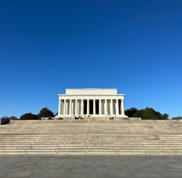 The Lincoln Memorial, a large white building with columns in front of of a blue sky