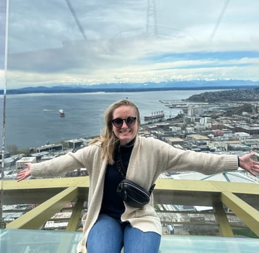 a woman on top of the space needle with the puget sound and olympics in the background