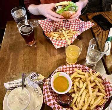 a person holding a cheeseburger with clam chowder and curry fries on the table