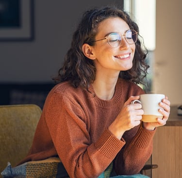 a woman in glasses and a sweater is smiling and holding a cup of coffee after individual counselling