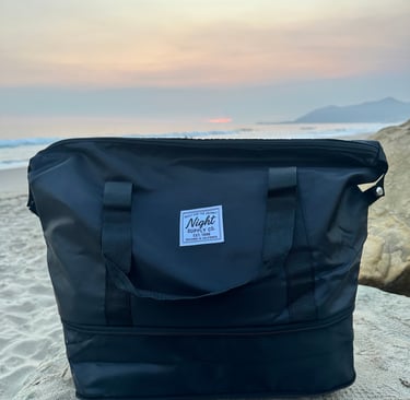 Black Night Supply Co. duffel bag on beach sand with sunset sky in background