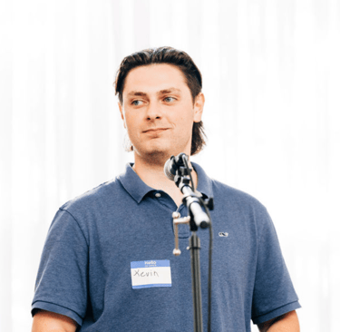 Kevin Bockius wearing a collared shirt, standing in front of a microphone giving a speech