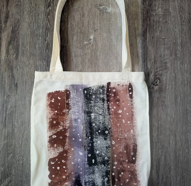 Hand-painted canvas tote bag with abstract plum and sage stripes, shown filled with groceries in a s