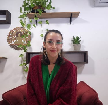 Mulher de óculos e brincos olhando para a câmera sorrindo com plantas e buda ao fundo