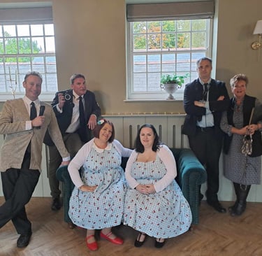 A group of event staff and performers in vintage 1950s attire posing for a photo at a retro-themed party.