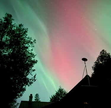 Green and pink northern lights with silhouette of a house with a satellite dish. Image by me.