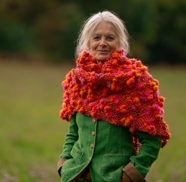 a woman in a green jacket and a red scarf . Triloom gewebter Schal aus Artyarn in orange und pink.