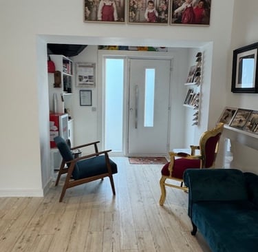 Modern home entryway with wood flooring, velvet chairs, and framed family portraits on a white wall.
