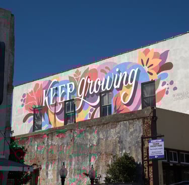 A colorful floral mural with the words Keep Growing painted on the side of a downtown brick building.