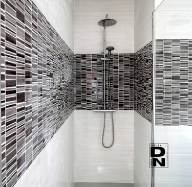 Instalación de ducha empotrada con mampara de cristal y revestimiento de azulejos grises y blancos en baño moderno. Proyecto 
