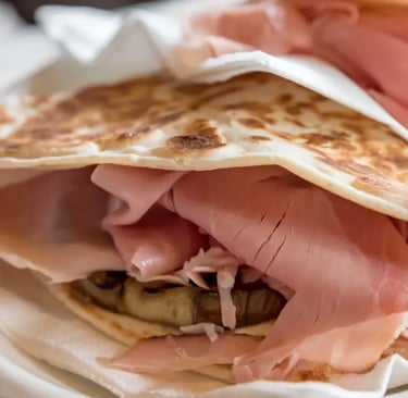 a plate of piadina romagnola with a sandwich and a fork and knife on it