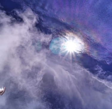 Gravity, Rainbows, and Destiny: Welcome to Phenomena. A hooded woman holding living light in her hand under a sunlit sky.