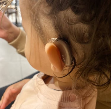 дитина в рожевому светрі зі слуховим апаратом