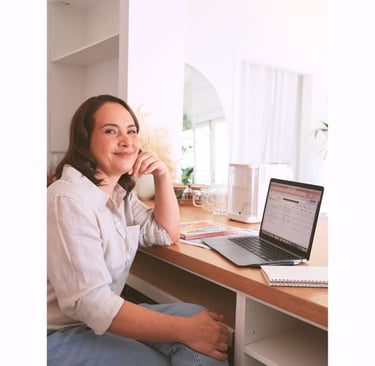 Milly smiling while working on a laptop in a bright, organised home office.