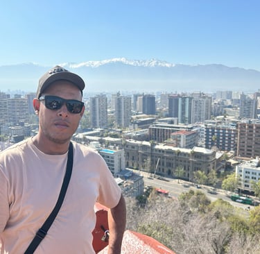 uma pessoa de óculos escuro de costa para a cidade e no fundo as cordilheiras dos andes no chile