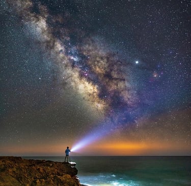 Galaxy of starts in night sky with lone man holding flashlight