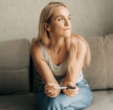 Woman sitting on couch holding a pregnancy test, reflecting on fertility questions