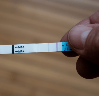 Positive LH ovulation test strip held in hand over wooden background