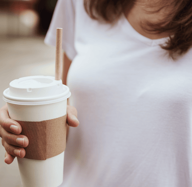 Close-up of woman in white shirt holding takeaway coffee cup
