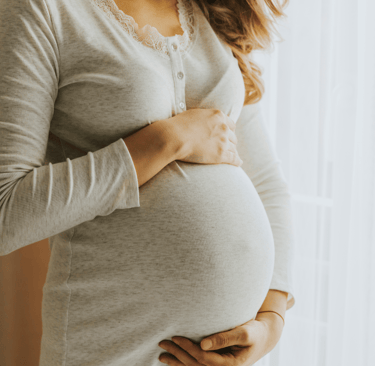 Pregnant woman standing by window with hands on belly