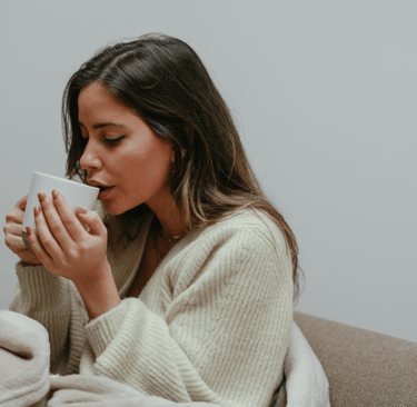 Woman wrapped in a cozy blanket holding a mug, sitting on a couch
