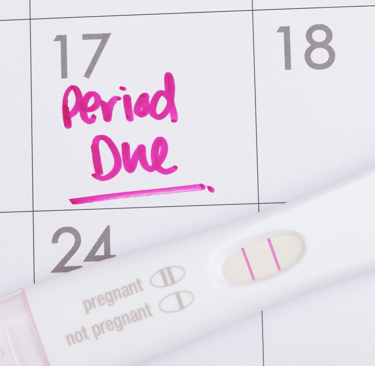 Calendar with "Period Due" written on it and a pregnancy test lying on top.