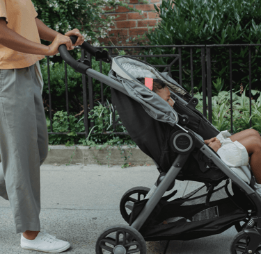 Parent pushing baby stroller outdoors on a sunny day