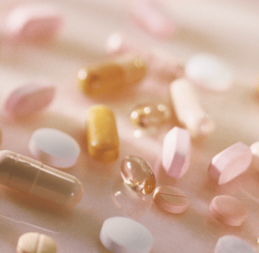 Close-up of assorted fertility supplements and capsules in soft, pinkish lighting.