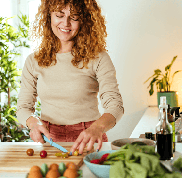 Smiling woman chopping vegetables in a bright kitchen with plants and fresh produce