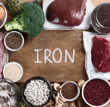 Flat lay of iron-rich foods like meat, spinach, beans, and seeds on a kitchen table
