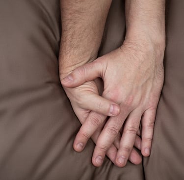 Two male hands entwined together on top of bedsheets