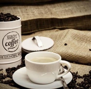 A professional image of an overflowing canister of coffee beans and a cup of milky coffee on an empty hessian bag