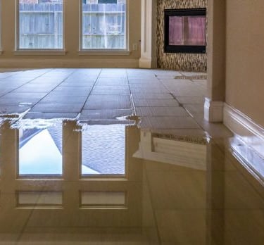 Flooded tiled living room with water damage after a plumbing failure, illustrating the risks of delayed insurance claims.