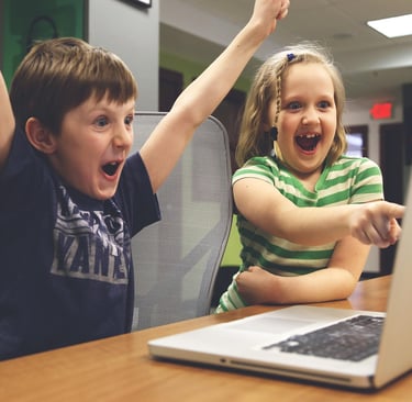 Two children happily looking at a laptop while planning a trip to Greece