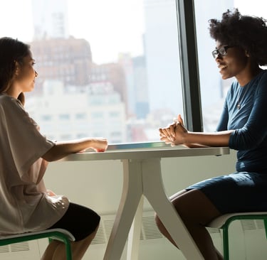 two women sitting at a table with a view of a city doing interview