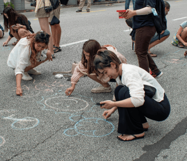 Children drawing and learning on the ground during an outdoor creative activity.