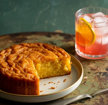 an orange semolina cake on a plate with a Wee Scottish Daisy cocktail