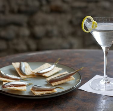 anchovies on water crackers plated on a rustic table next to a Dry Martini with a lemon twist