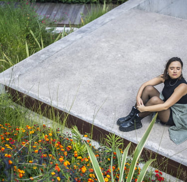 A stylish woman sitting on a concrete rooftop garden with vibrant wildflowers and green plants.