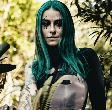 Alternative woman with green hair and gothic makeup posing in a forest.