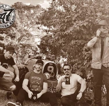 Acorde 7 Blues Band members posing with a vintage classic car in a sepia-toned outdoor portrait.