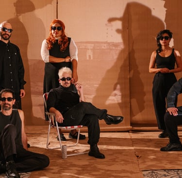 A diverse musical band wearing sunglasses posing against a cardboard backdrop with dramatic shadows.