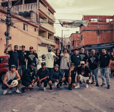 A group of Brazilian hip-hop artists posing in a neighborhood street with urban buildings.