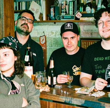 A group of young punk rock fans wearing band t-shirts sitting at a bar with drinks.