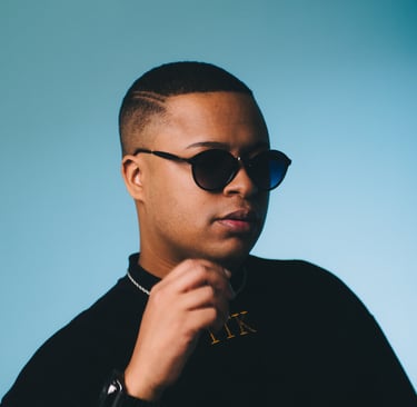 Young man with a faded haircut wearing black sunglasses and a gold chain on a blue background.