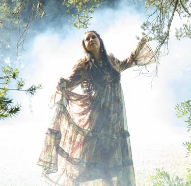 A woman in a flowing bohemian maxi dress stands in a misty, ethereal forest setting with natural sunlight.