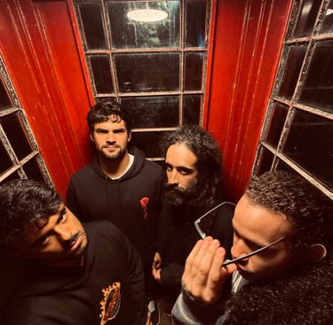 Four men in black hoodies posing inside a vintage red telephone booth with atmospheric lighting.