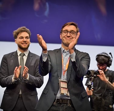 Two business professional men in suits clapping on stage during a corporate event or conference.